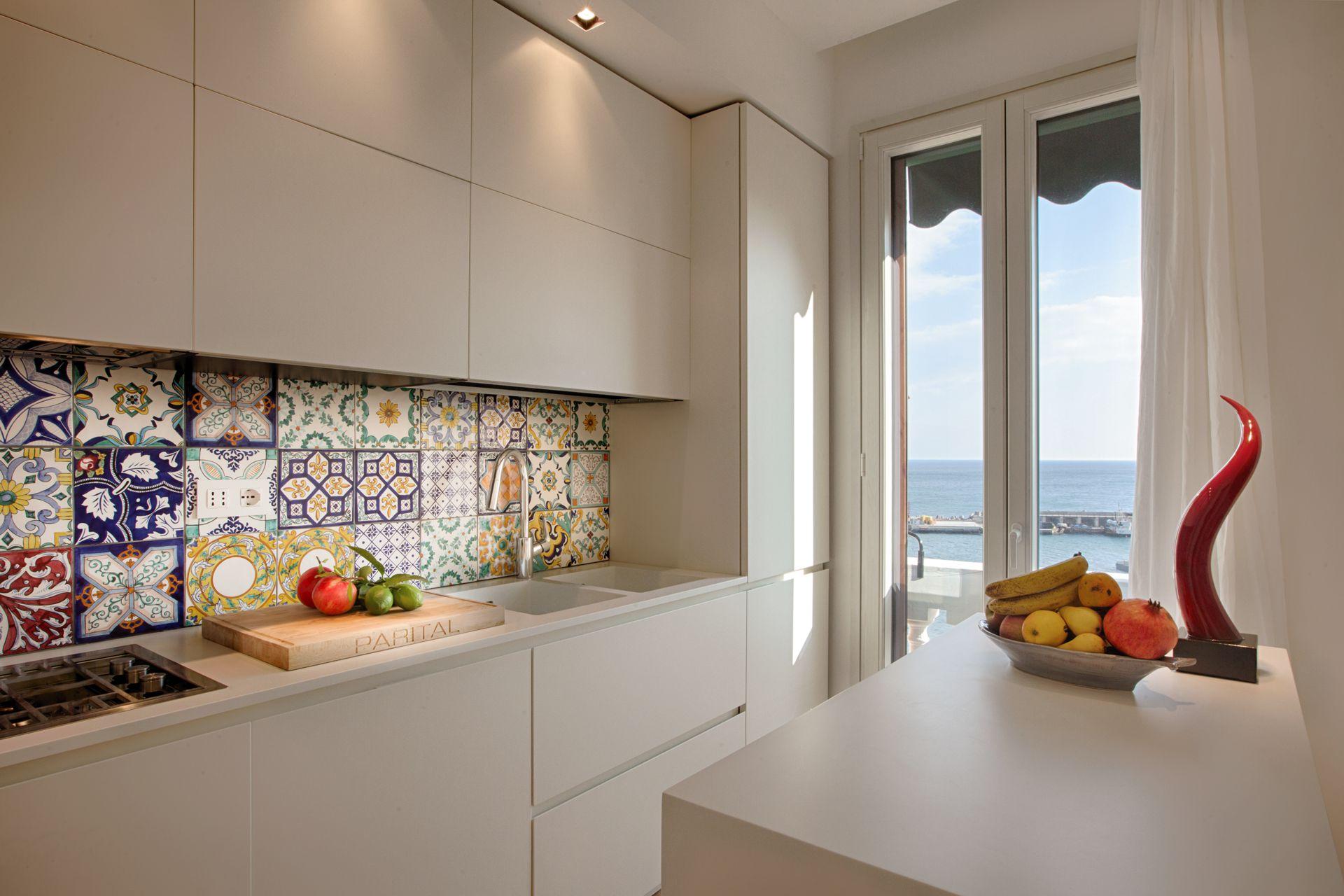 Prosjekt for interi&oslash;r og eksteri&oslash;r av Ernesto Fusco p&aring; Amalfikysten. Detalj av kj&oslash;kken med keramisk backsplash, integrerte skap og vindu som rammer inn utsikten over Middelhavet.